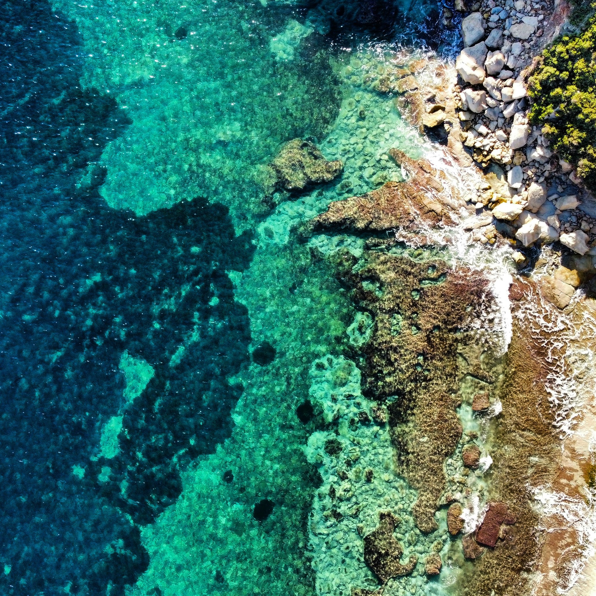 Aerial view of clear turquoise water meeting the rocky Delimara coast